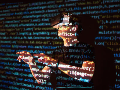 Double exposure of a caucasian man and Virtual reality VR headset is presumably a gamer or a hacker cracking the code into a secure network or server, with lines of code